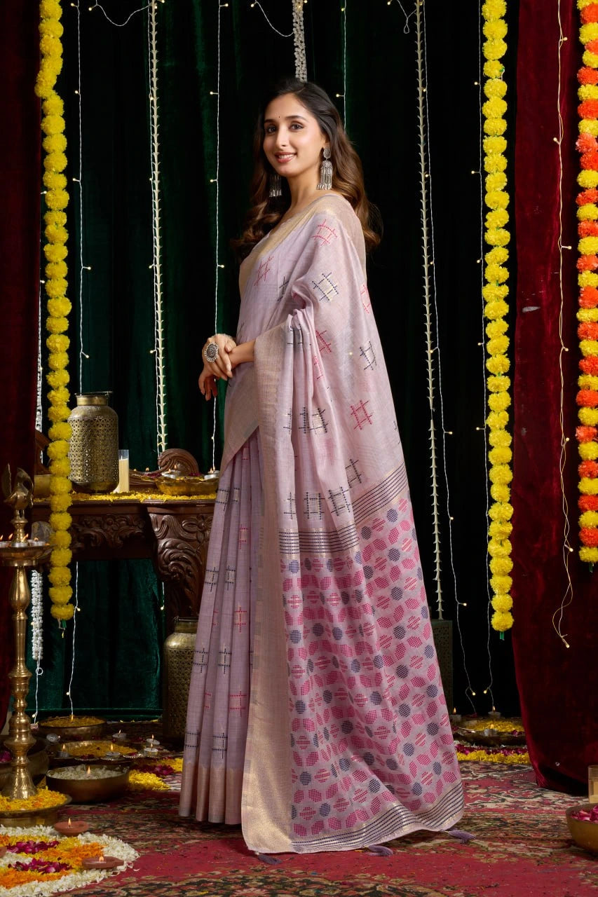Woman in a pink saree with floral patterns standing in a decorated indoor setting.