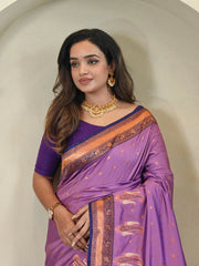 Woman wearing a purple saree with gold jewelry against a neutral background