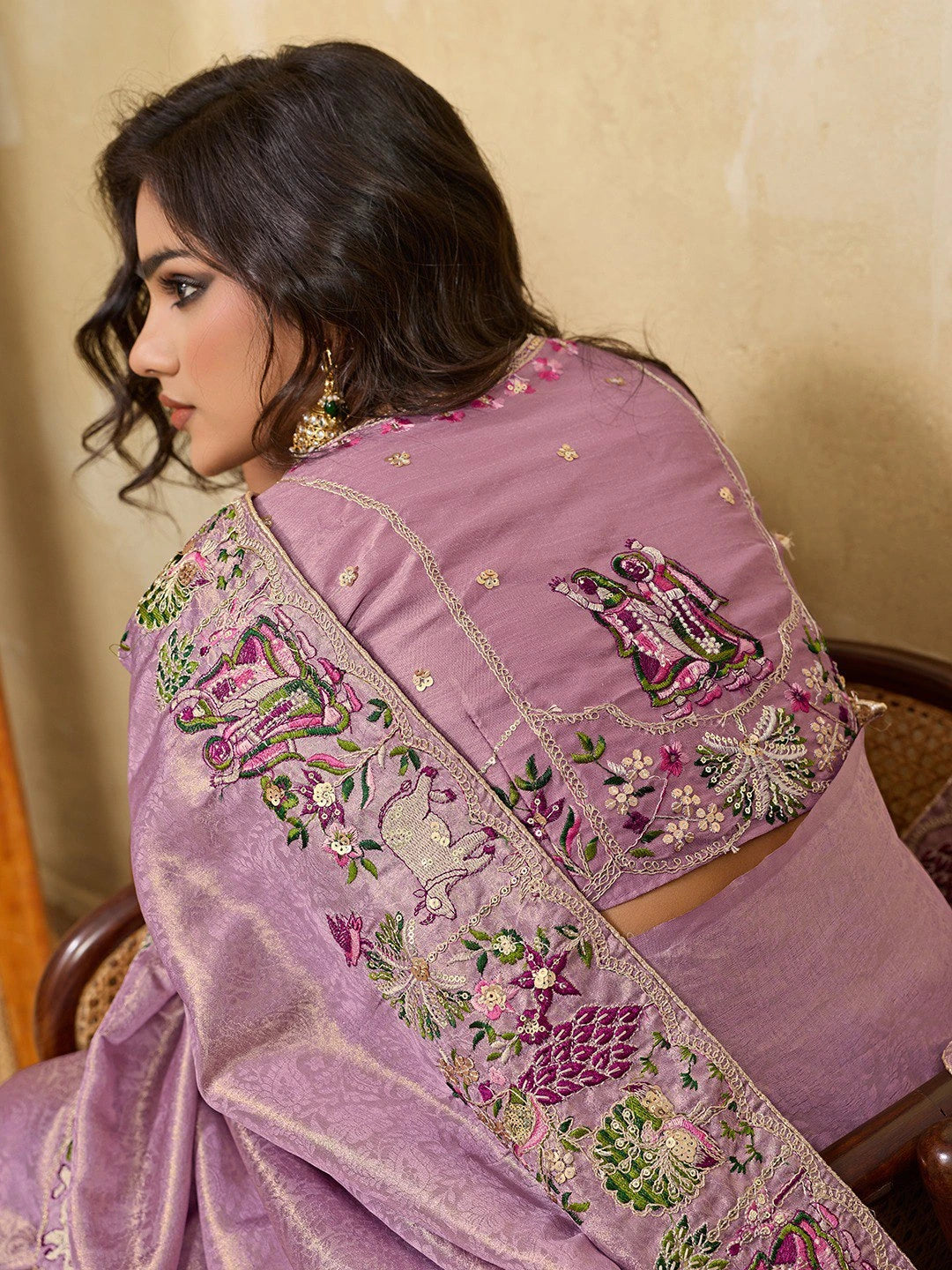 Woman wearing a purple saree with intricate embroidery, sitting on a chair.
