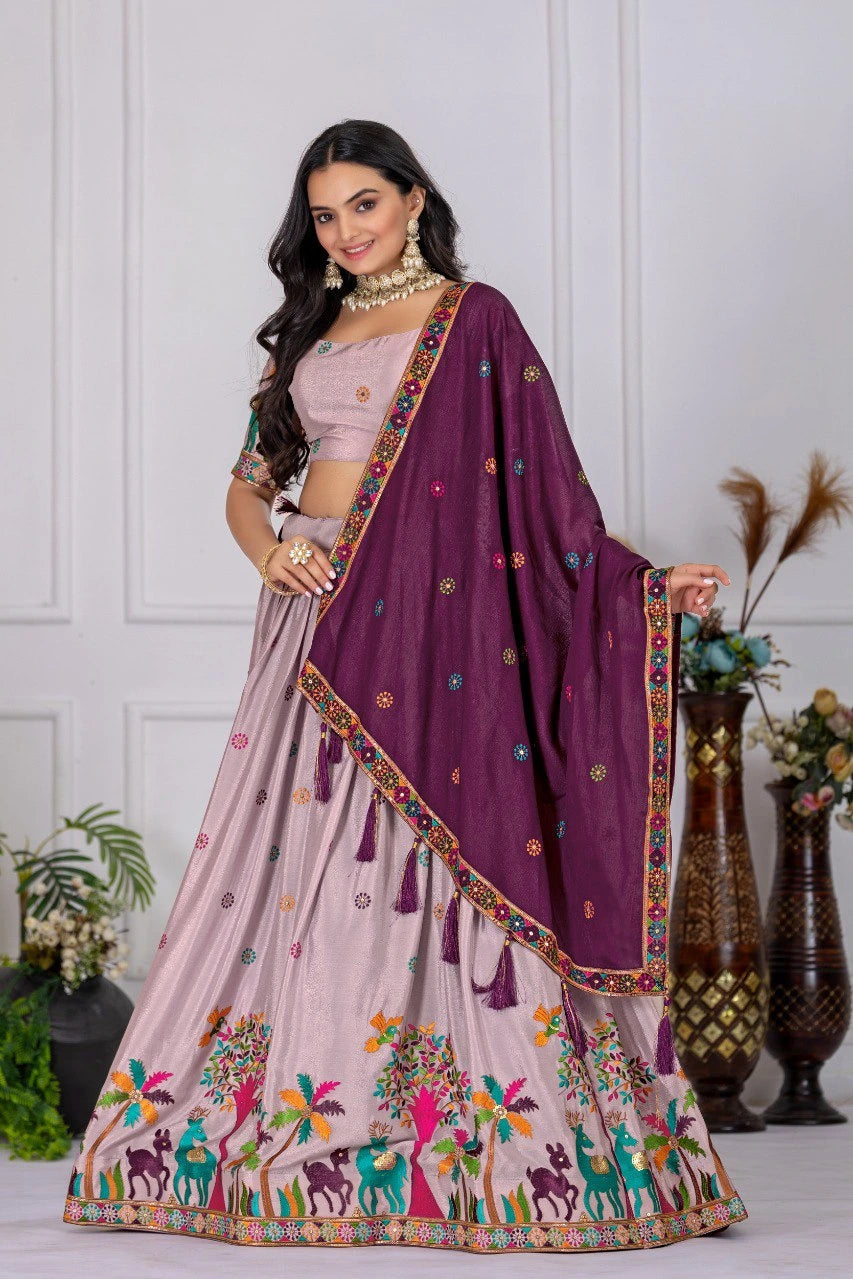 Woman wearing a traditional outfit with a purple dupatta and colorful skirt against a white wall.