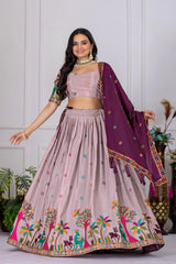 Woman wearing a traditional outfit with a pink lehenga and purple dupatta against a white wall.