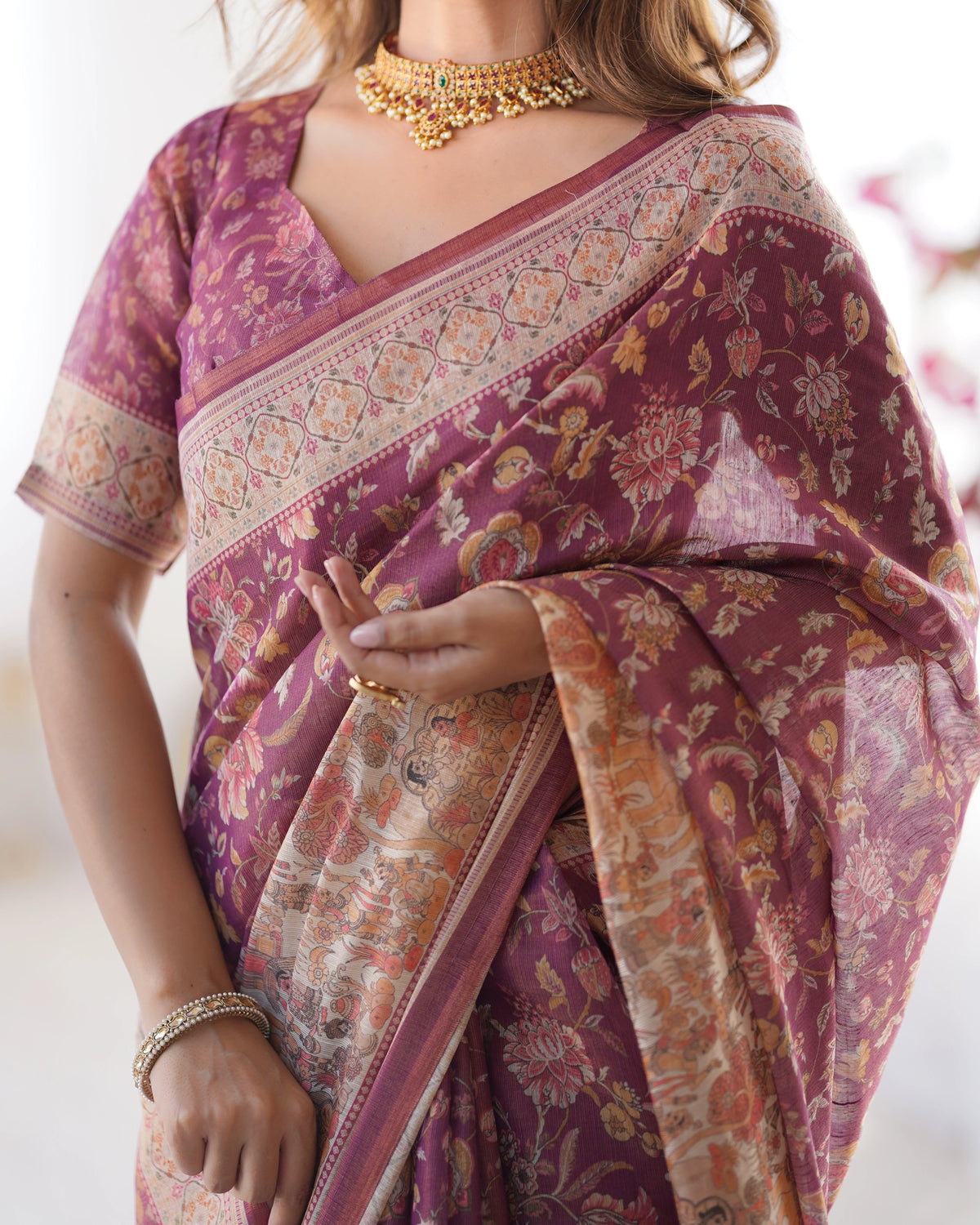 Woman wearing a purple saree with floral patterns and gold jewelry.