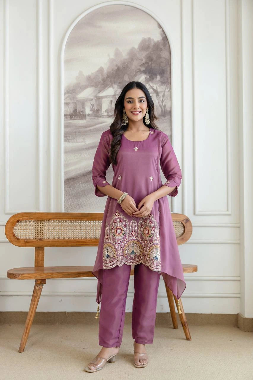 Woman in a purple traditional outfit standing in a room with a wooden bench and framed picture.