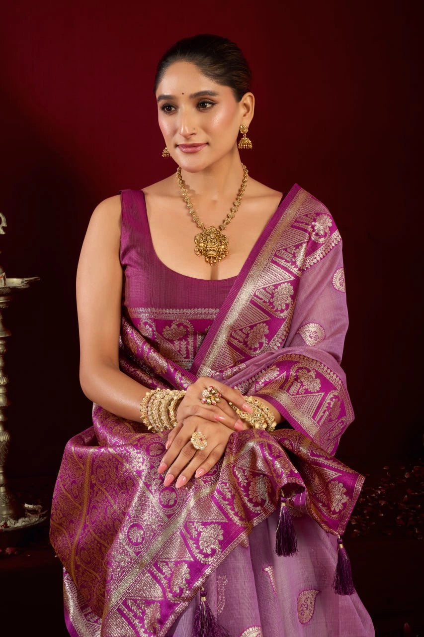 Woman in a traditional purple saree with gold jewelry against a dark background