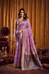 Woman in a pink saree with intricate designs standing against an orange curtain backdrop.