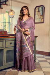 Woman in a purple saree with floral patterns standing in a room with a mirror and cabinet.