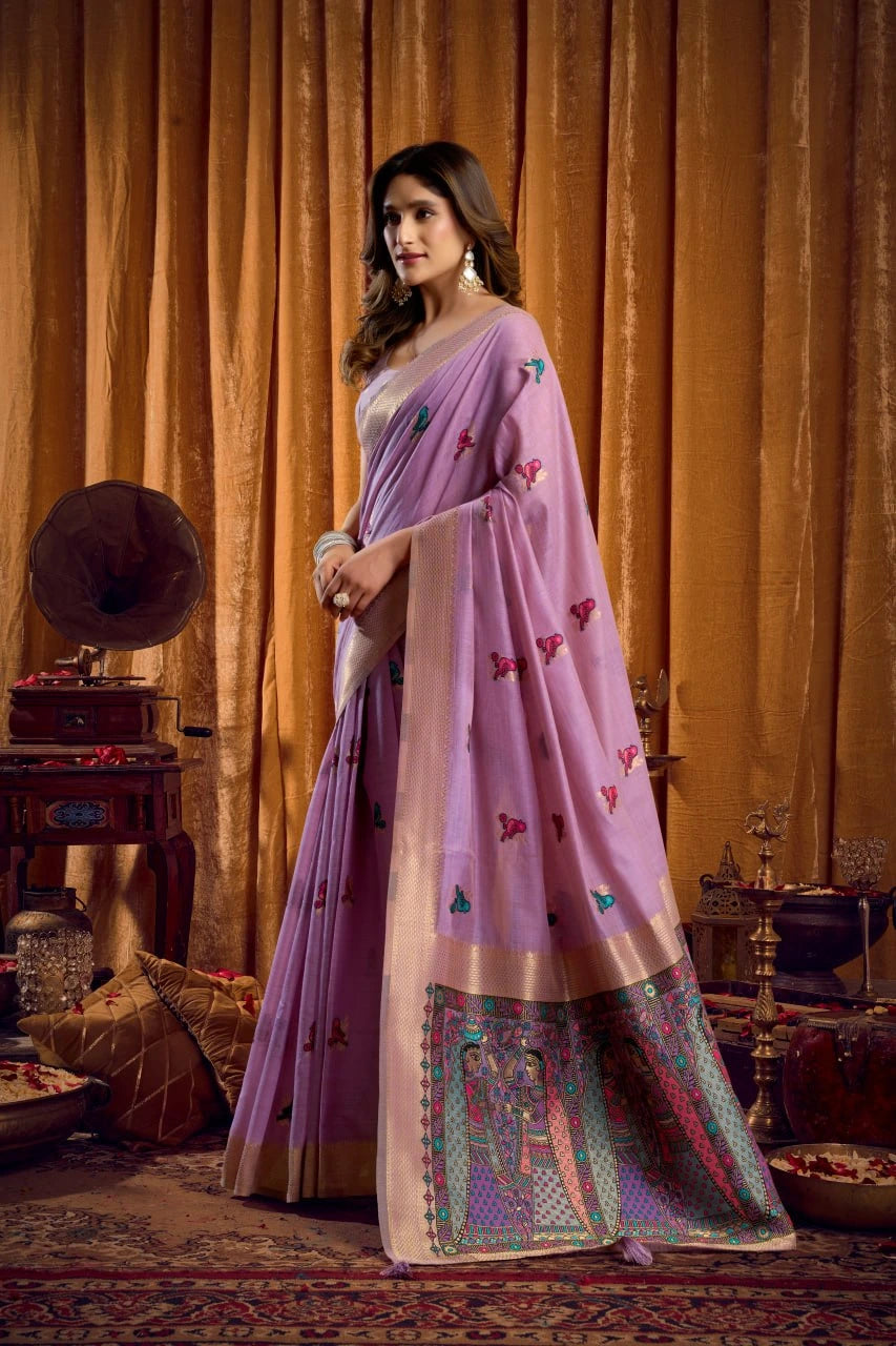 Woman in a pink saree with intricate patterns standing in a room with vintage decor.