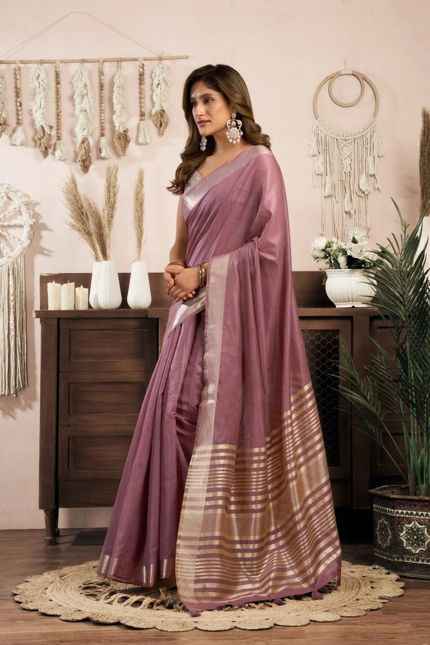 Woman in a mauve saree standing in a decorated room with plants and decor items.
