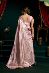 Woman in a pink saree standing on a staircase with red curtains and decorative items in the background.