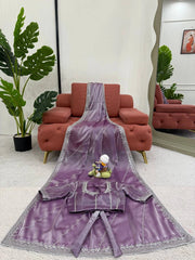 Purple saree with silver border on a white floor with red sofa and plants in the background