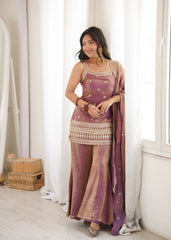 Woman in a traditional outfit standing in a bright room with white curtains.