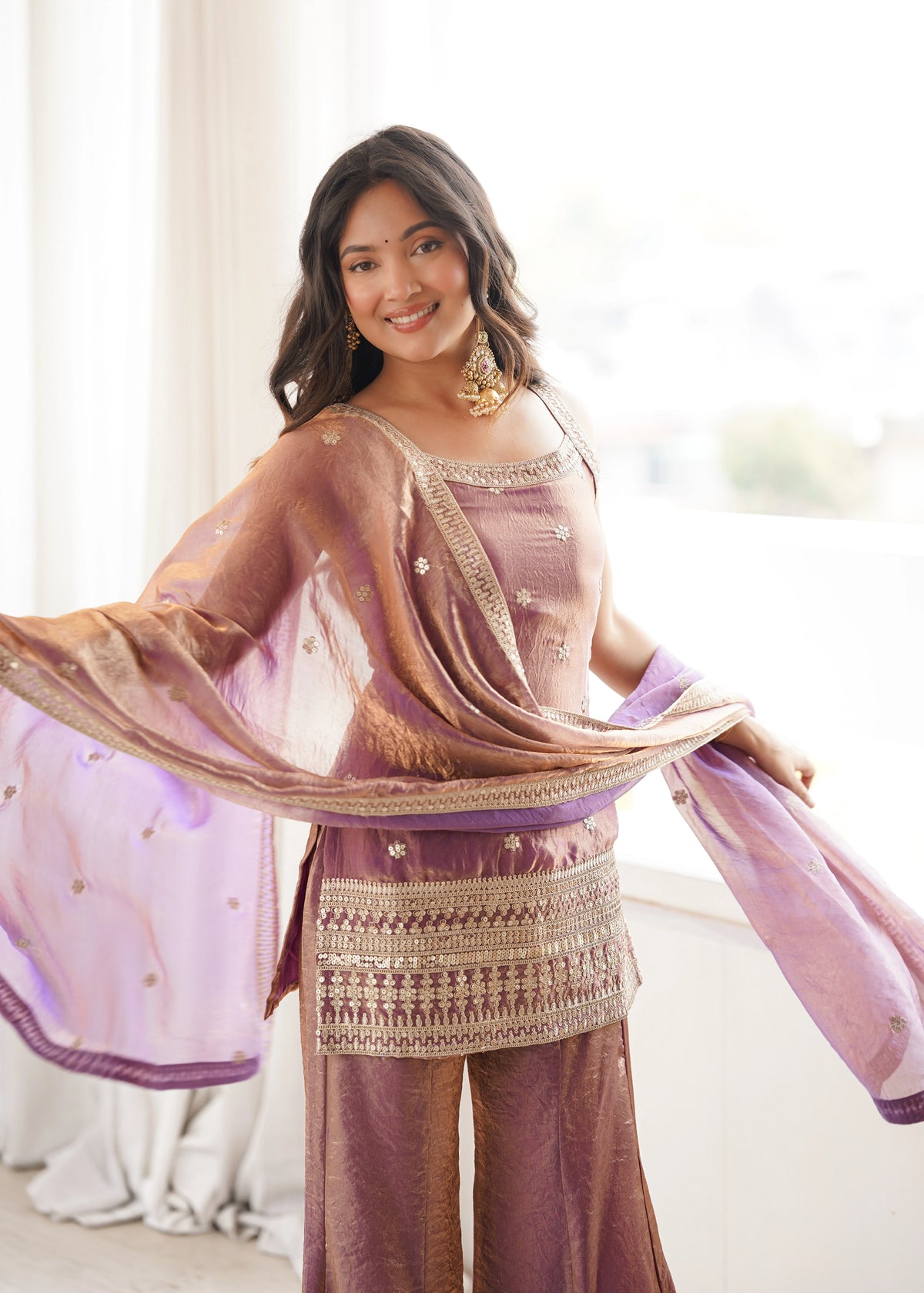 Woman wearing a traditional outfit with a pink dupatta in a bright room.