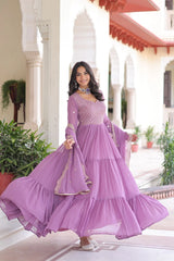Woman in a purple traditional outfit standing in an elegant indoor setting.