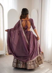 Woman wearing a purple traditional outfit with intricate designs, standing in a bright room.