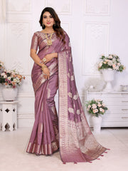 Woman wearing a purple saree with gold patterns in a decorated room.