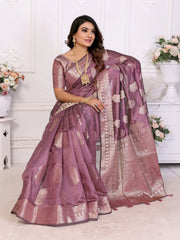Woman wearing a purple saree with gold patterns in a decorated room.