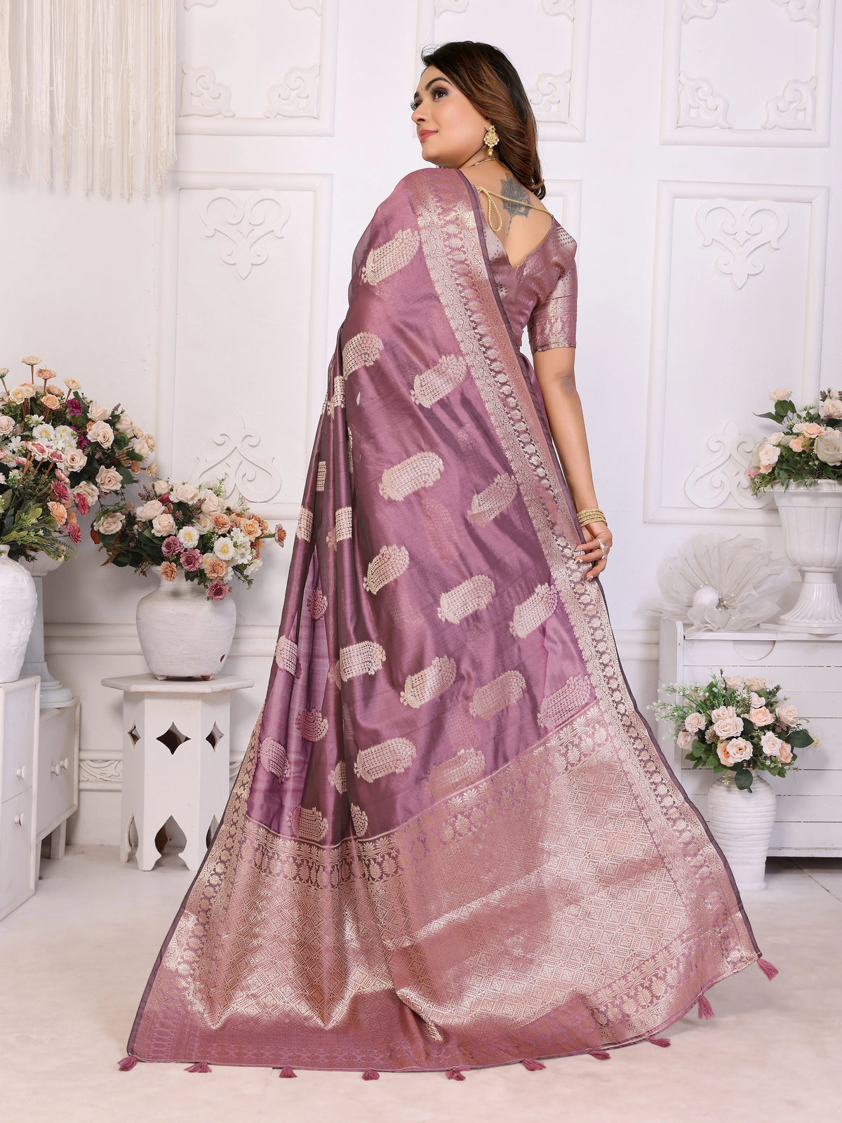 Woman wearing a purple saree with white patterns in a decorated room.