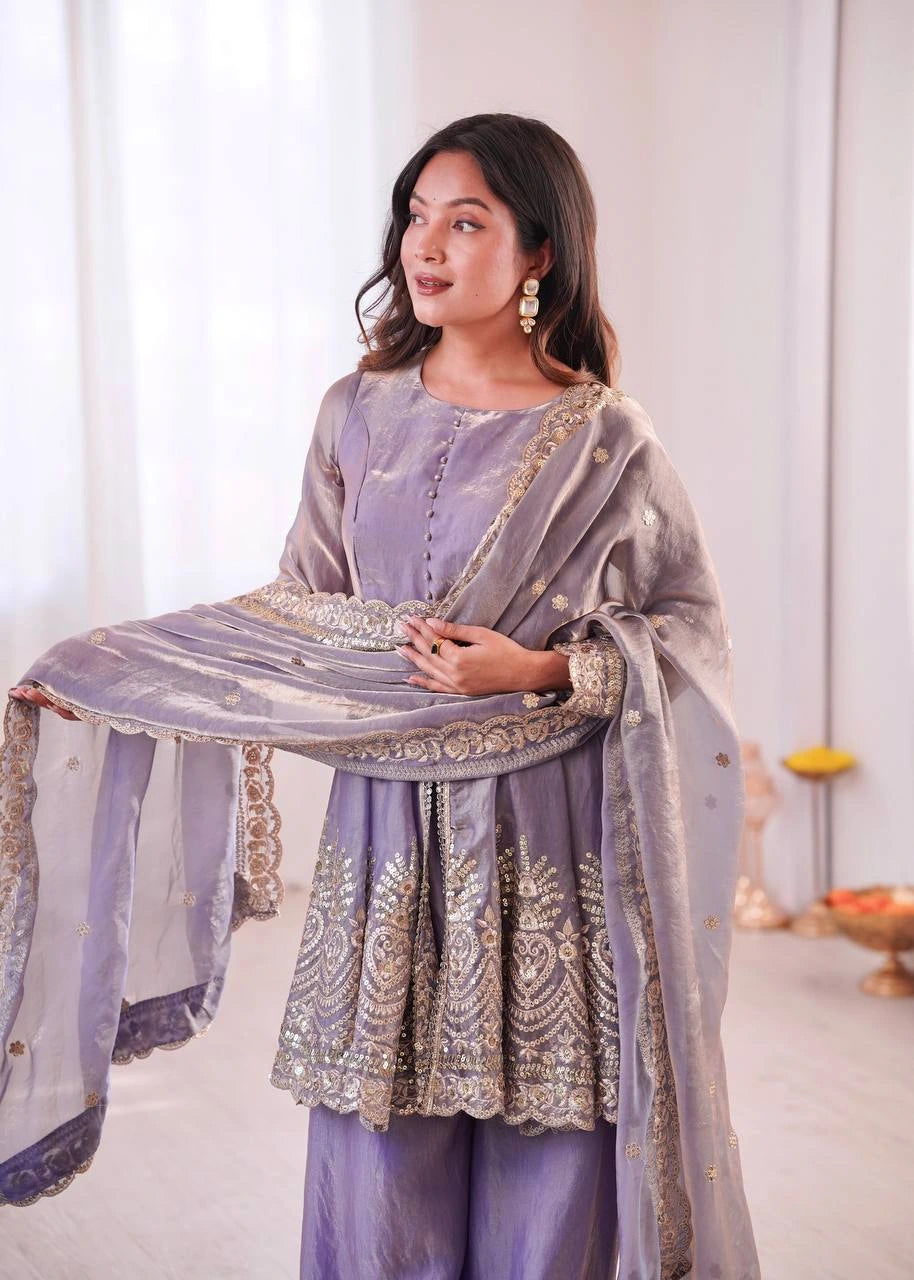 Woman in a lavender traditional outfit with a matching dupatta, standing against a white curtain.