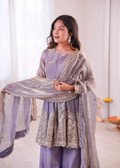Woman in a lavender traditional outfit with a matching dupatta, standing against a white curtain.