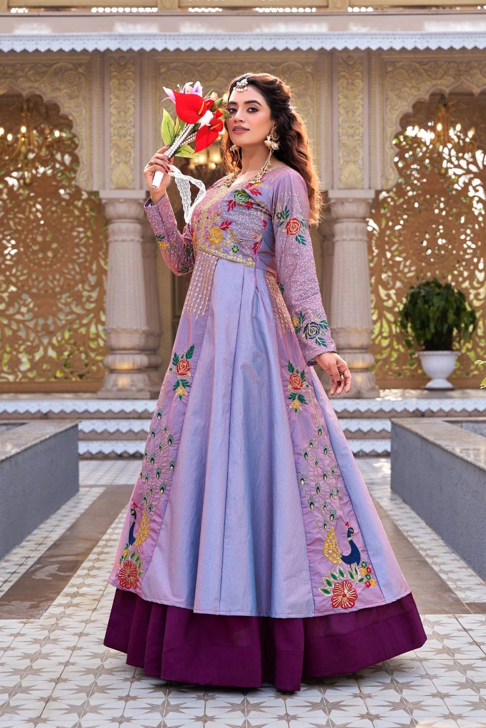 Woman in a traditional outfit with floral patterns holding a red flower in an ornate setting.