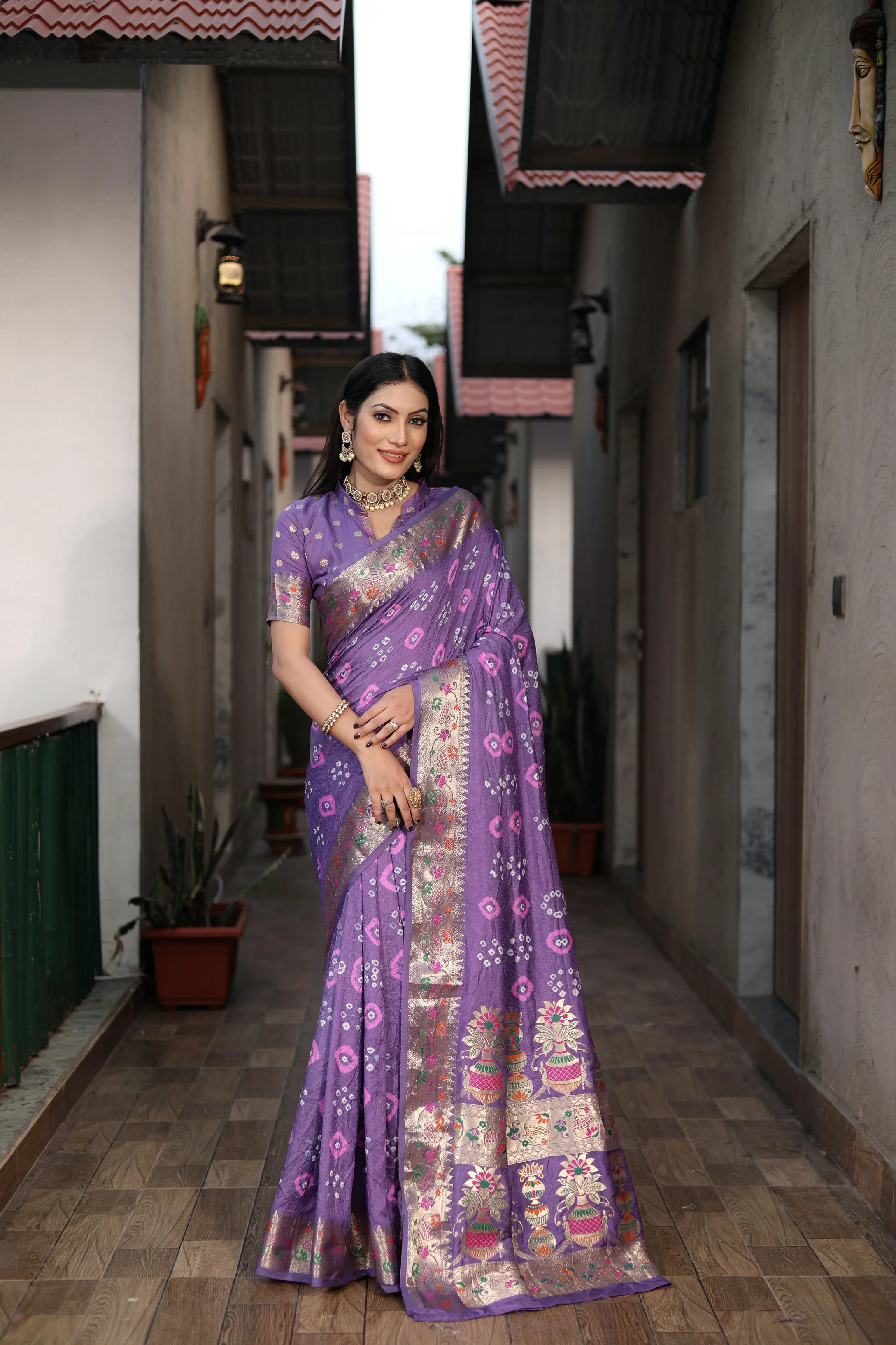 Woman in a purple saree standing in a narrow alleyway.