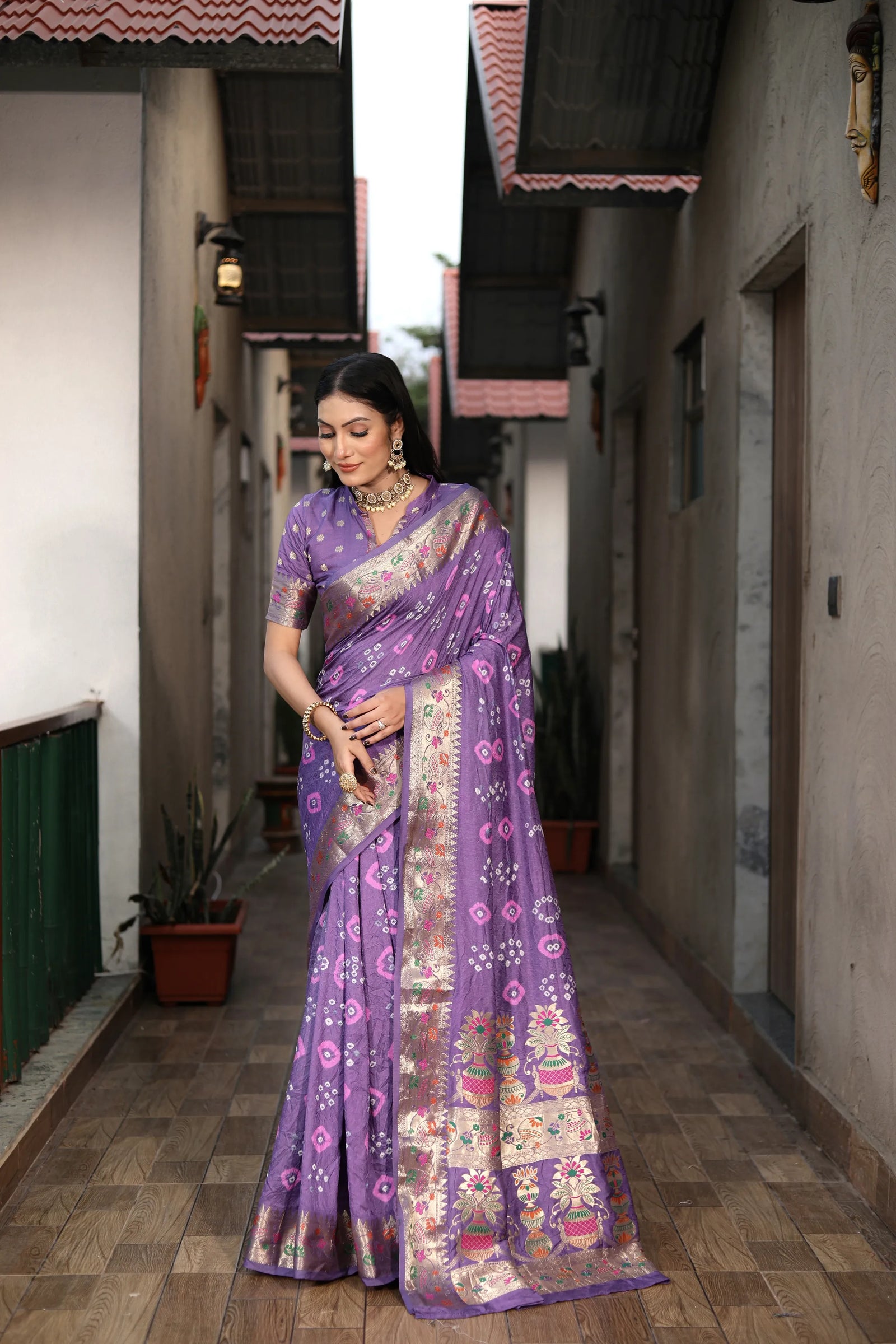 Woman in a purple saree with floral patterns standing in a narrow alleyway.