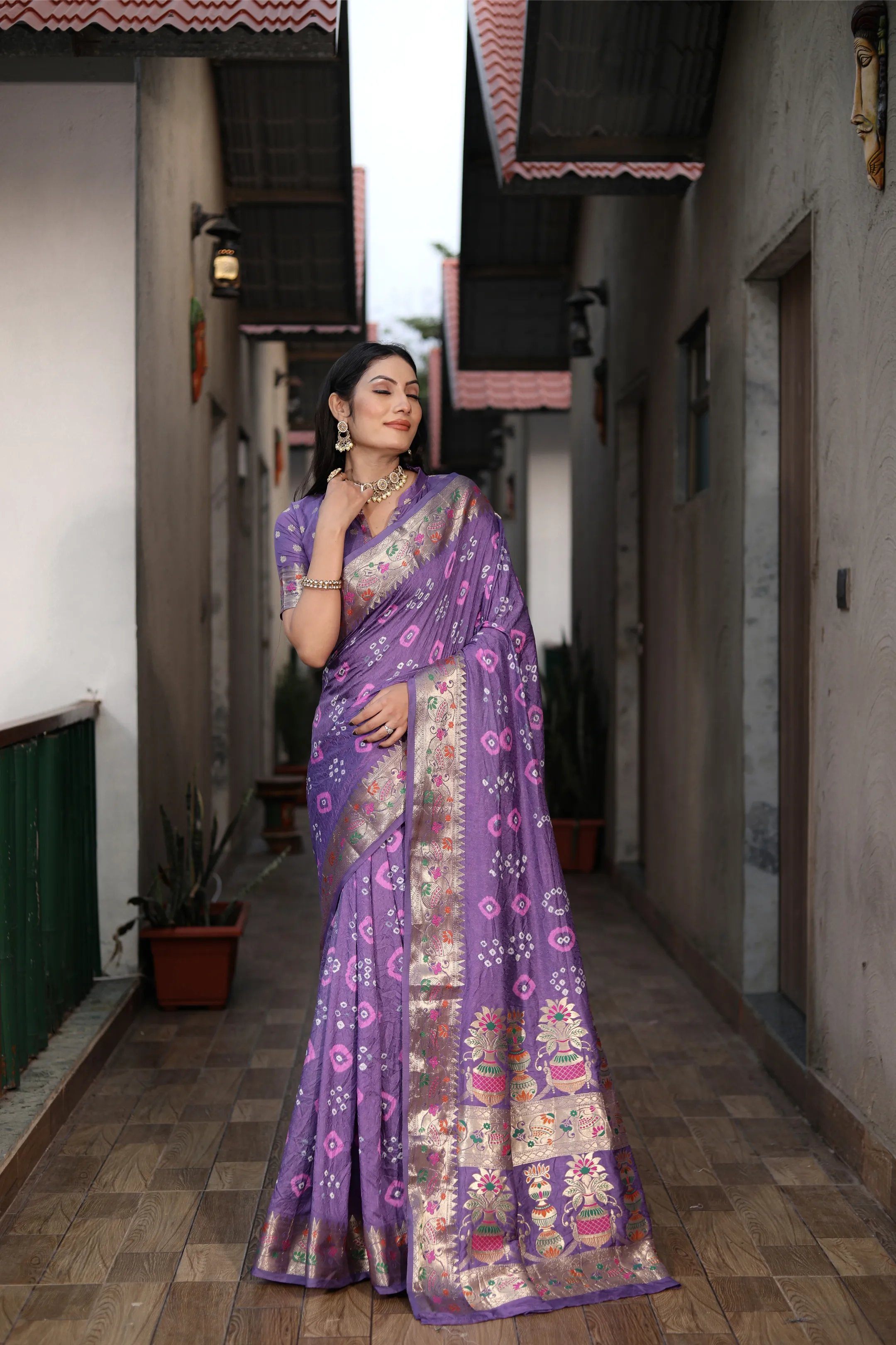 Woman in a purple saree standing in a narrow alleyway.