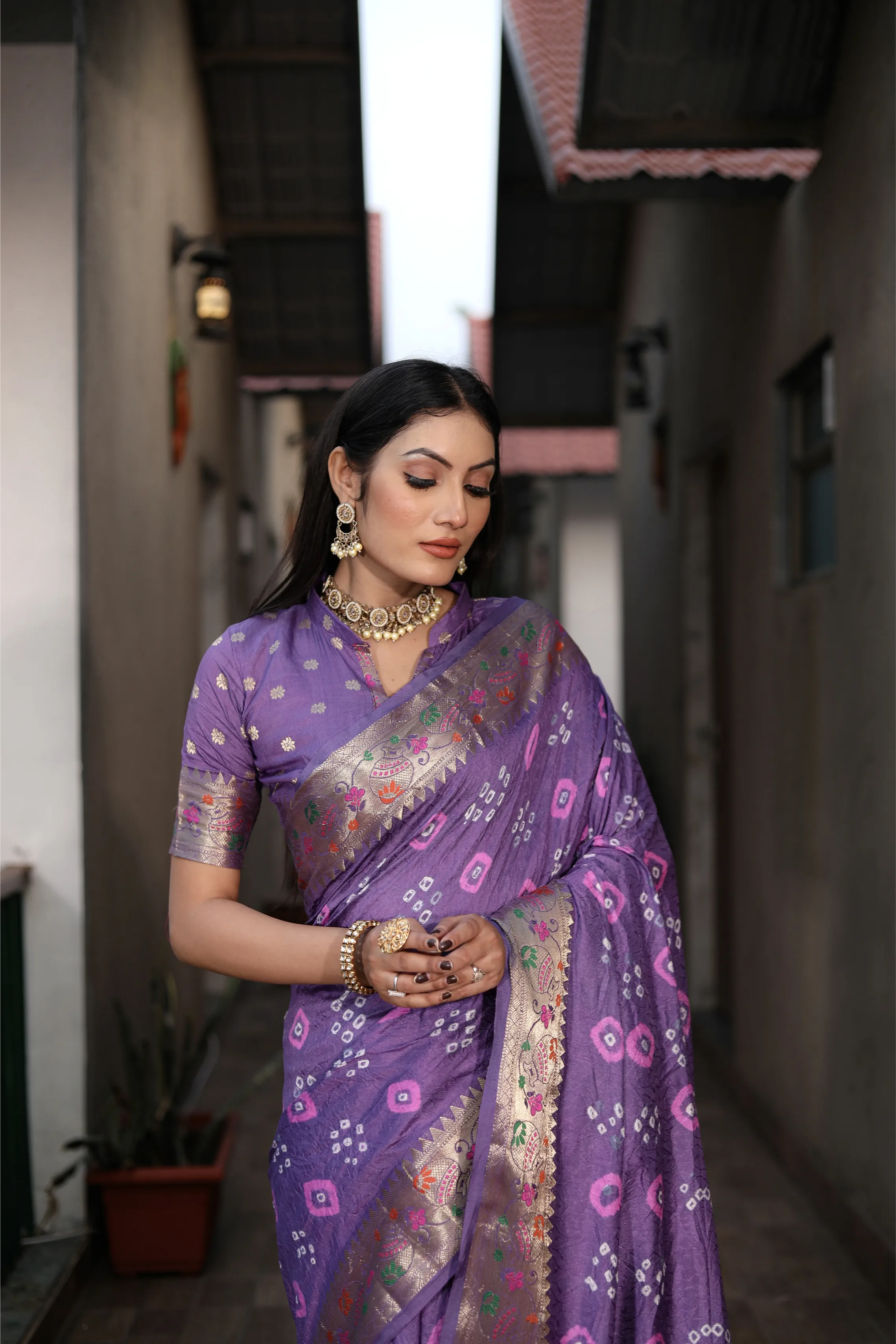 Woman wearing a purple saree with a patterned border in an outdoor setting.