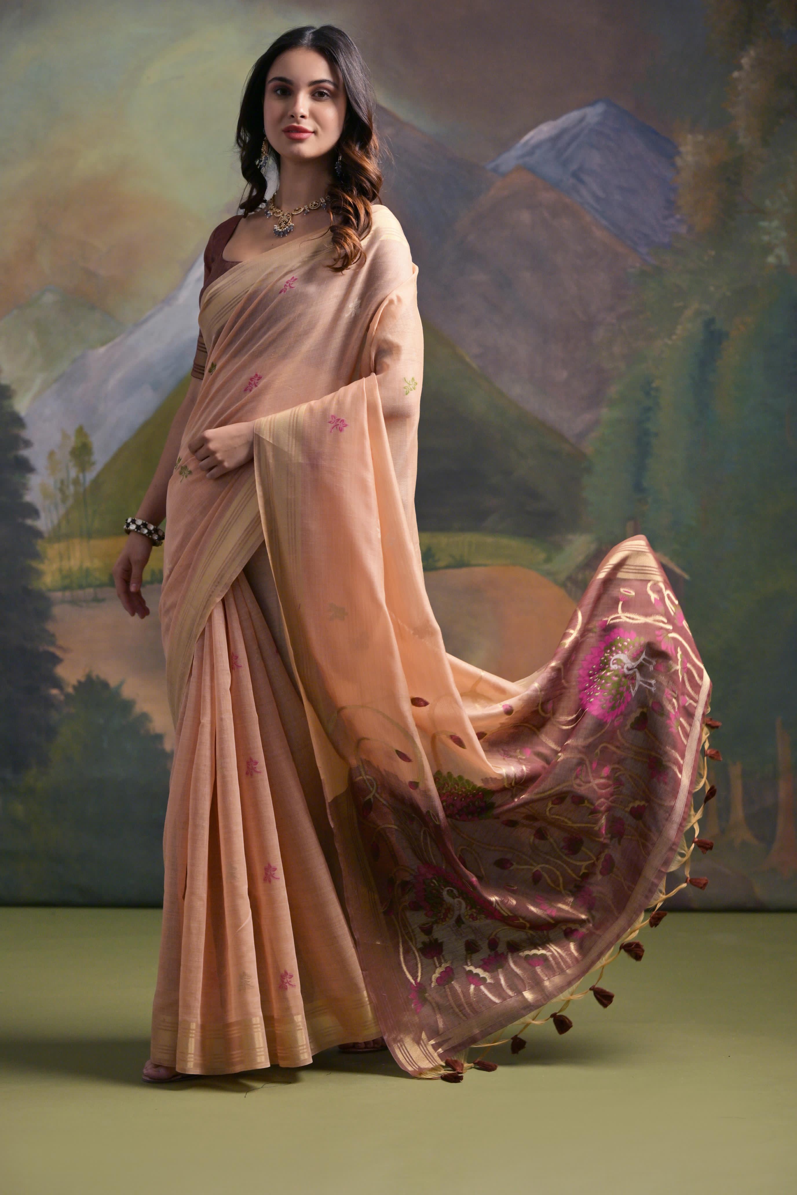 A woman models a soft Light Peach Muga Silk Saree with subtle Resham weaving. The pallu dramatically transitions to a dark brown/maroon color, featuring intricate pink and purple floral Resham threadwork. She wears a dark brown blouse and a gold Kundan necklace.