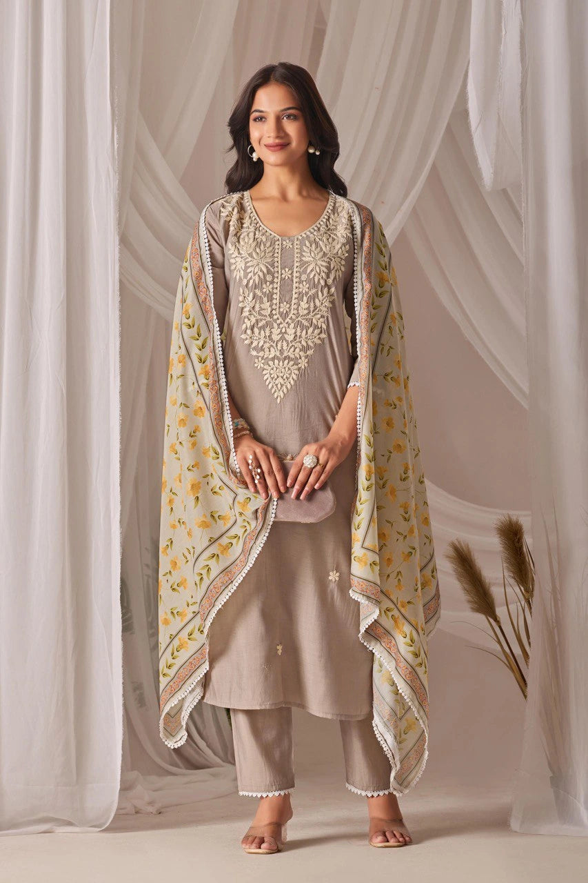 Woman wearing a traditional outfit with a beige kurta, pants, and a matching dupatta against a white curtain background.