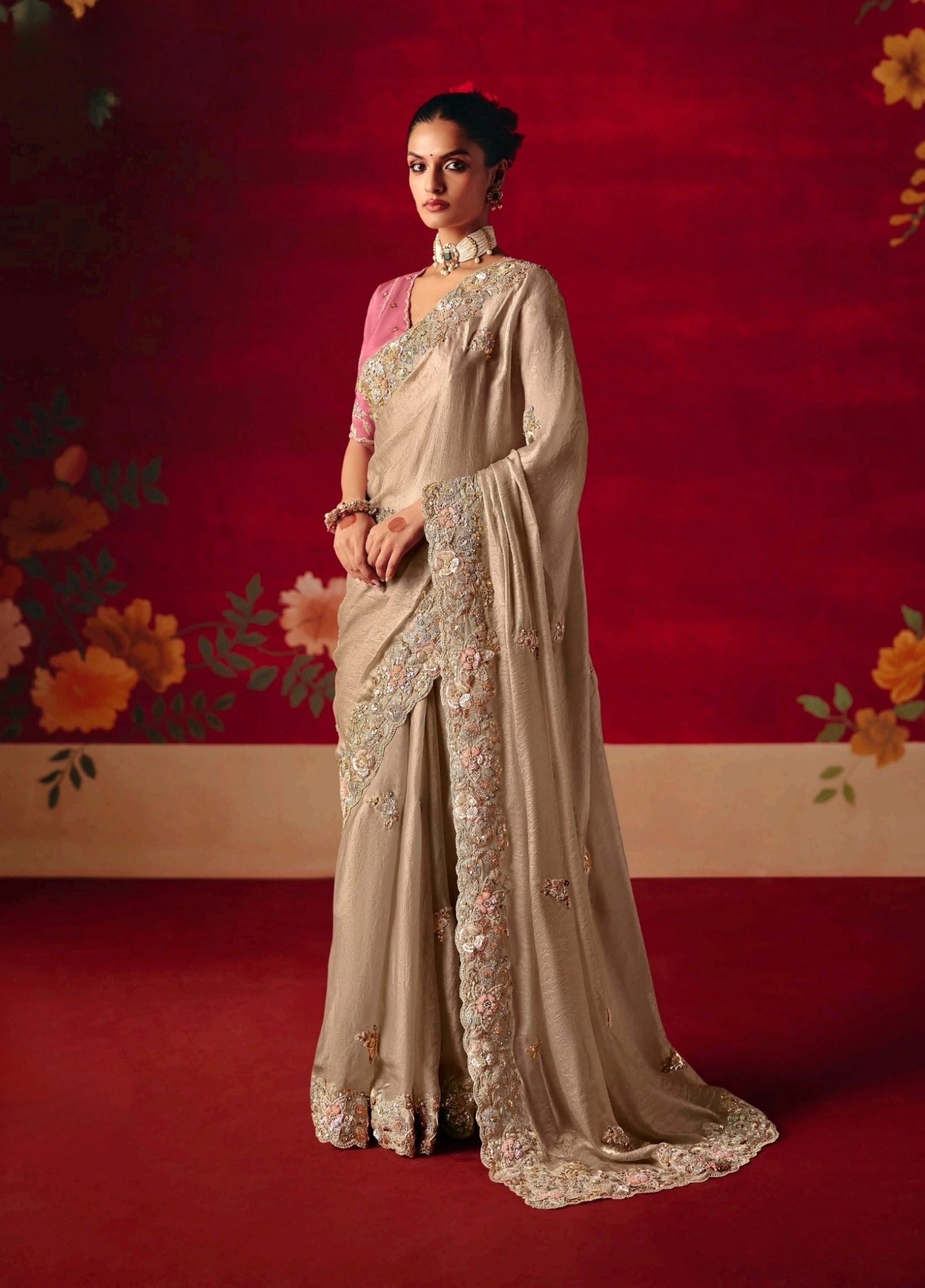 Woman in a beige saree with floral patterns against a red background