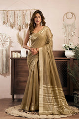 Woman in a gold saree standing in a decorated room with wooden furniture and decorative items.