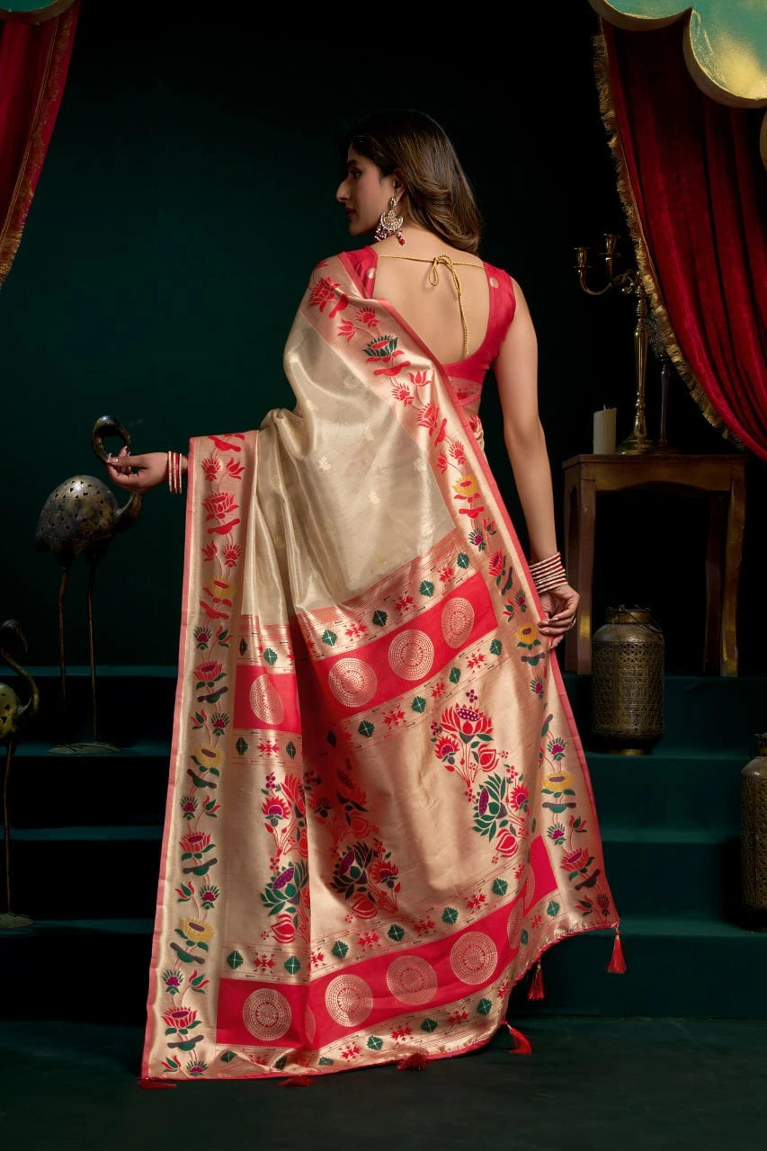 Woman in a traditional saree with a red and gold pattern, standing against a dark background.