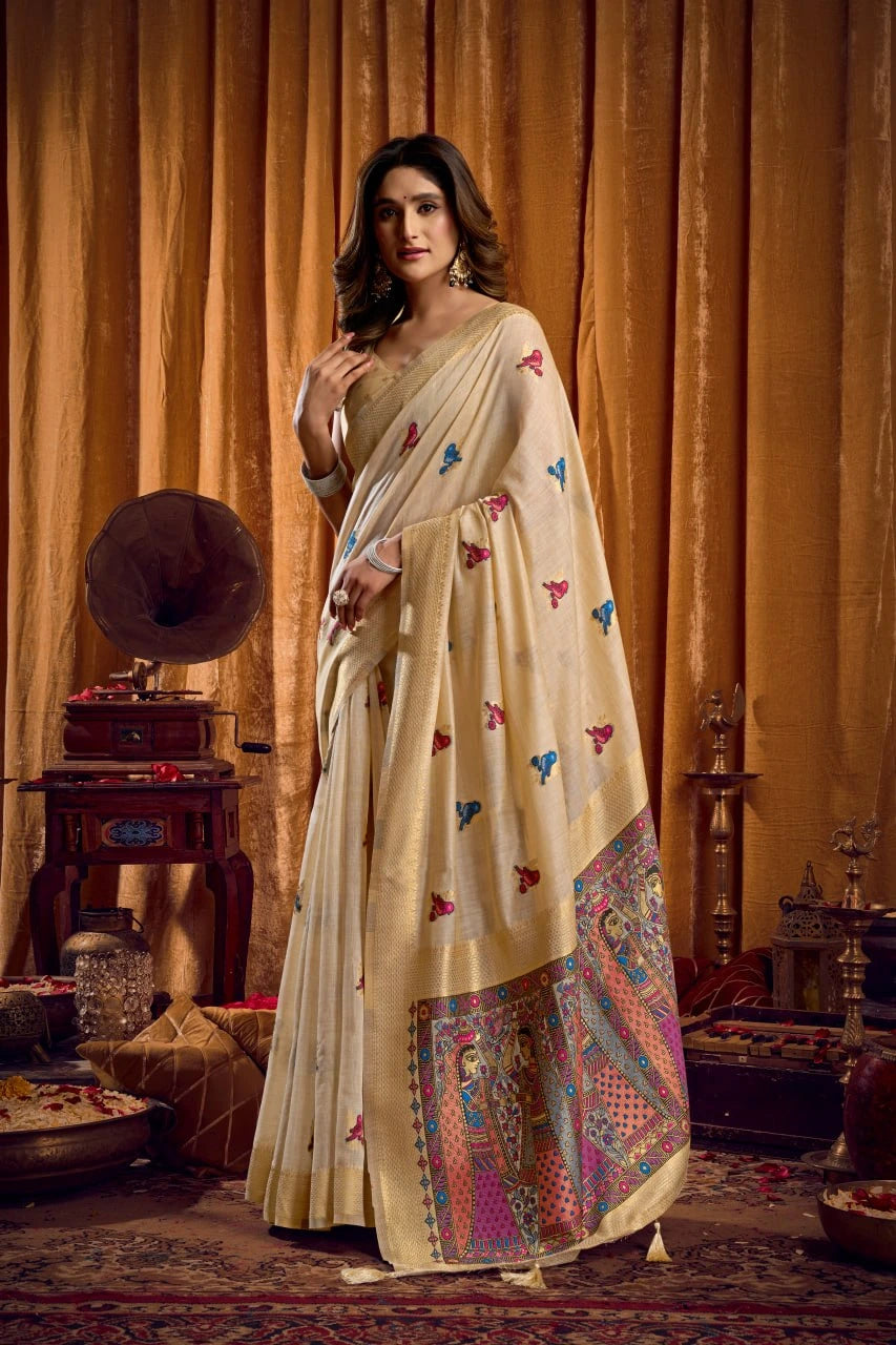 Woman in a cream saree with colorful patterns standing in a vintage room.