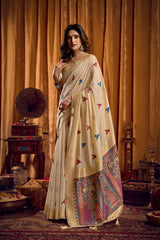 Woman in a cream saree with colorful patterns standing in a vintage room.