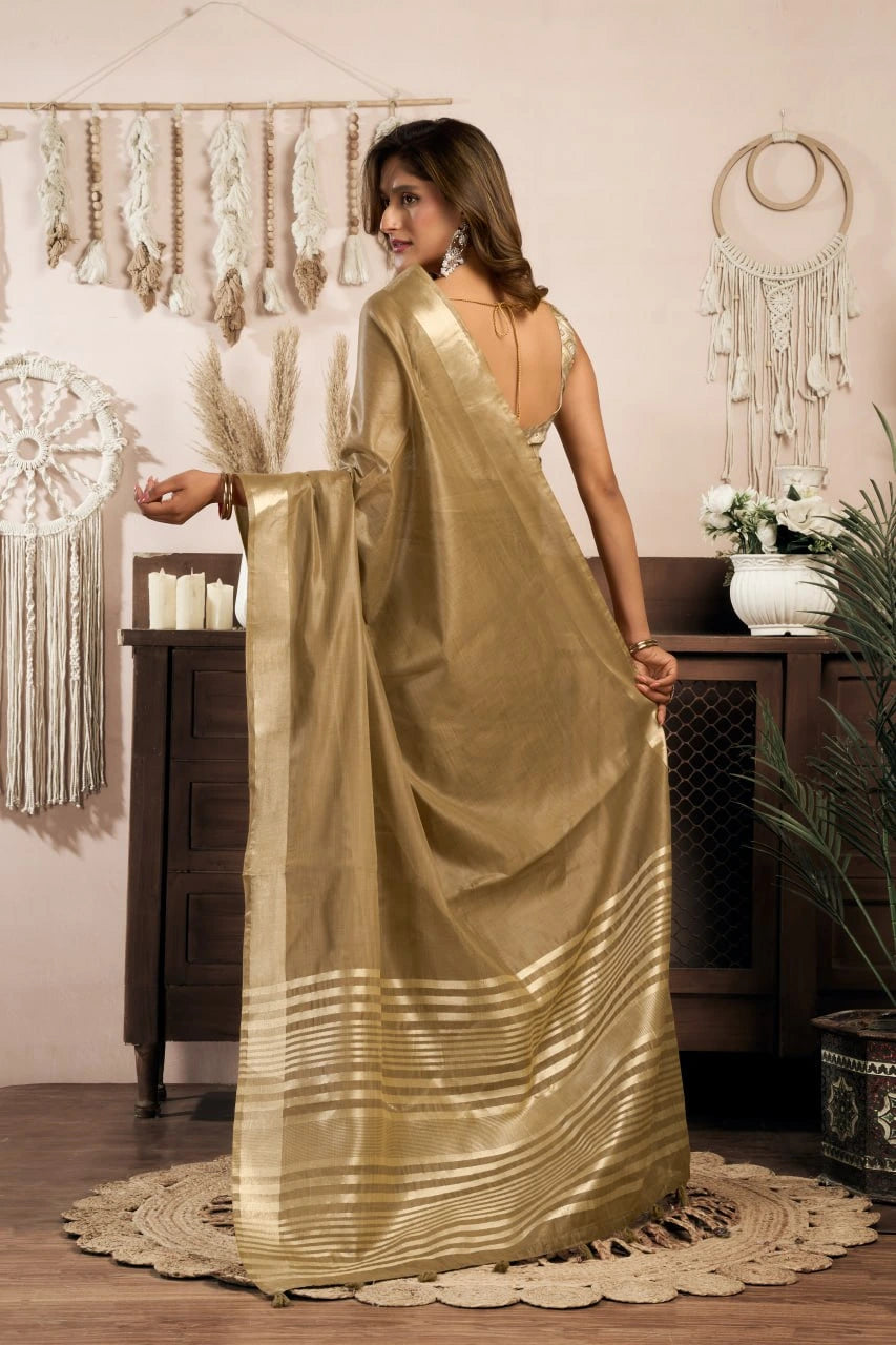 Woman in a gold saree standing in a room with decorative elements.