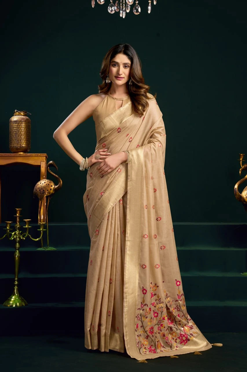 Woman wearing a beige saree with floral patterns in a dark setting