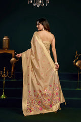 Woman in a beige saree with floral patterns standing in a dark room.