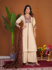 Woman in a traditional outfit with embroidery, standing against a brown wall with decorative elements.