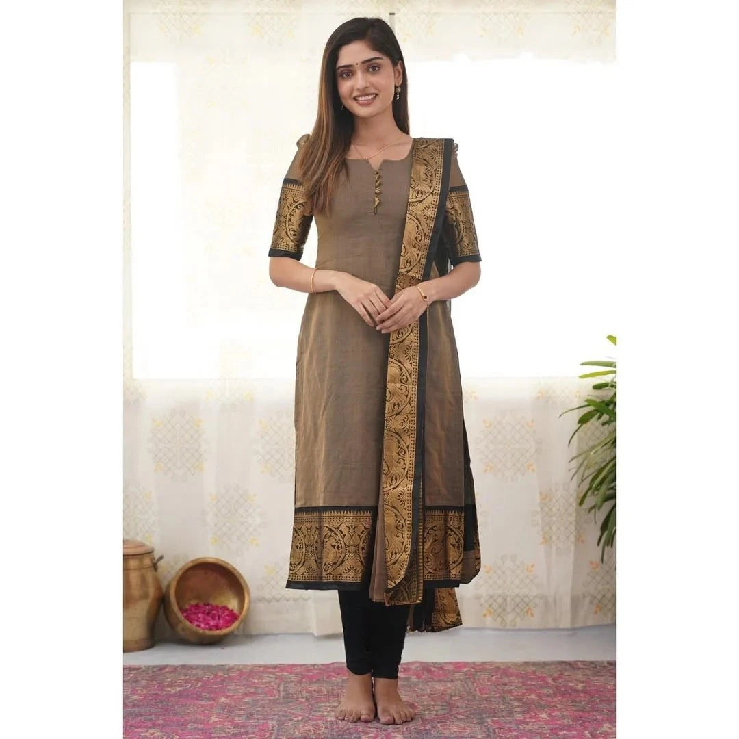 Woman wearing a brown and black traditional outfit with intricate designs, standing against a white wall.