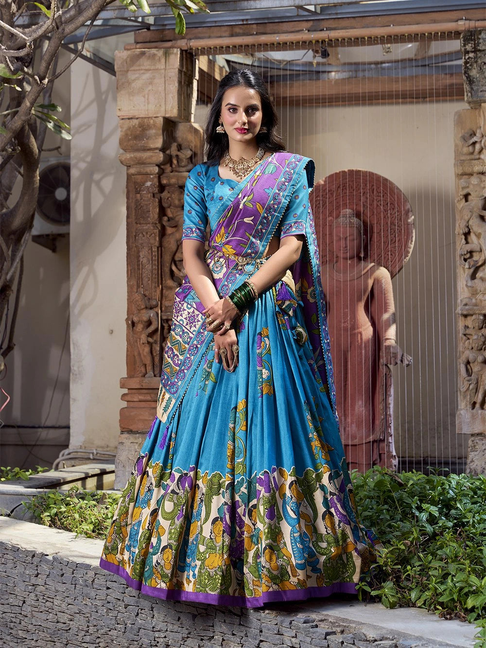 Stylish sky blue Kalamkari printed saree with colorful heritage motifs, purple border, and festive elegance.