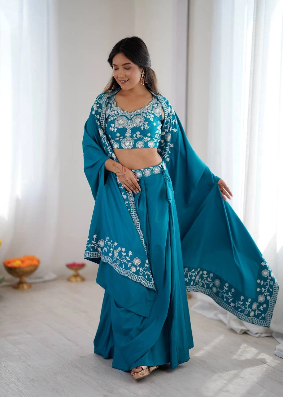 Woman in a teal traditional outfit with white embroidery standing in a bright room.