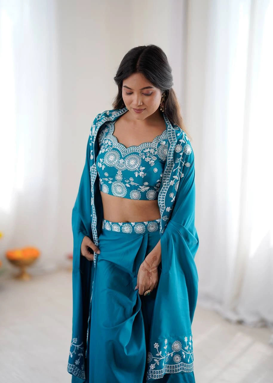 Woman wearing a traditional teal outfit with white embroidery in a bright room.