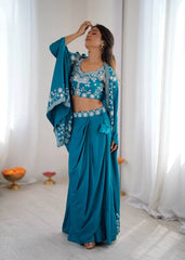 Woman in a teal traditional outfit with white embroidery standing in a bright room.