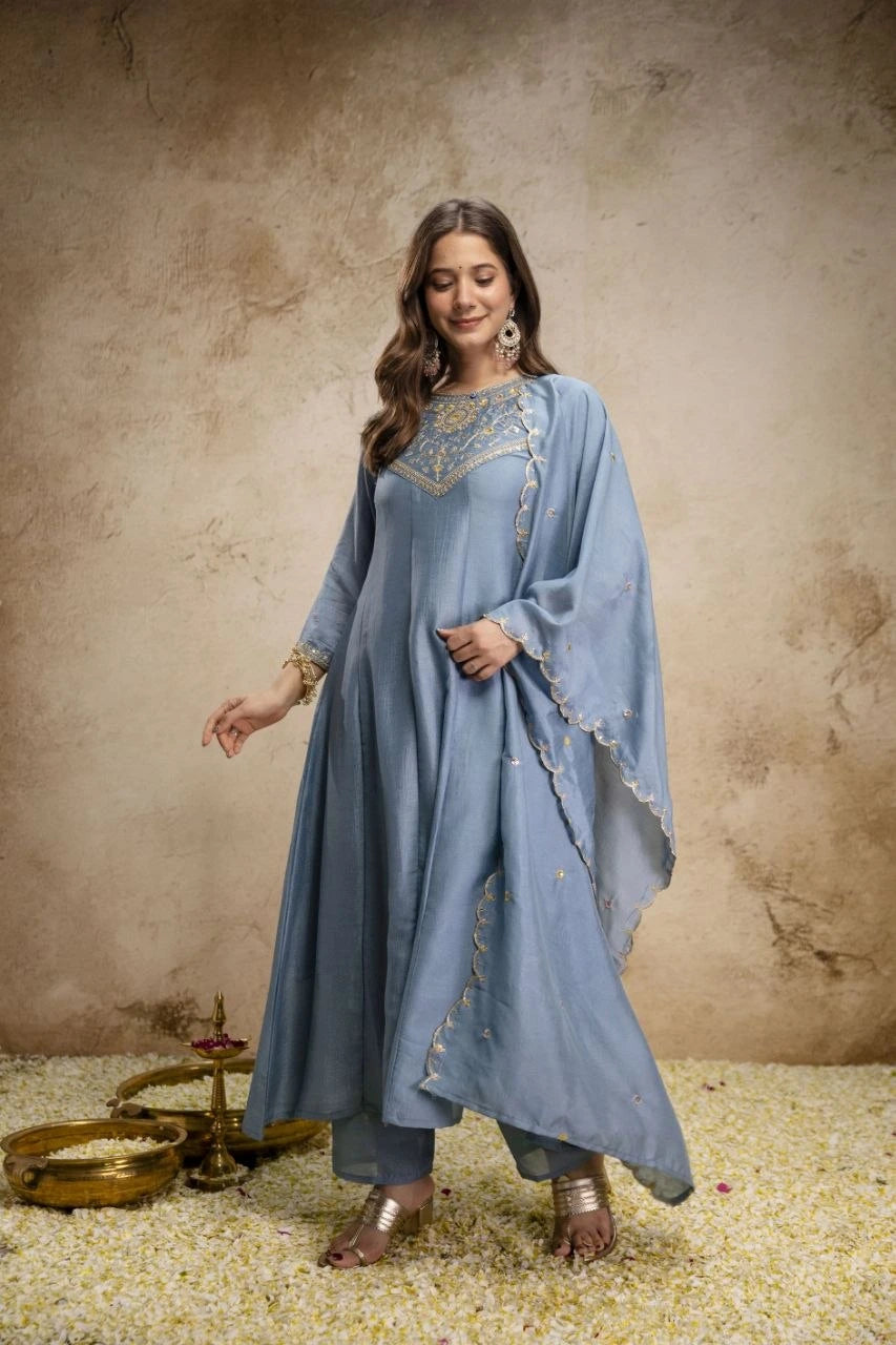 Woman wearing a light blue traditional outfit with intricate designs against a textured beige background.