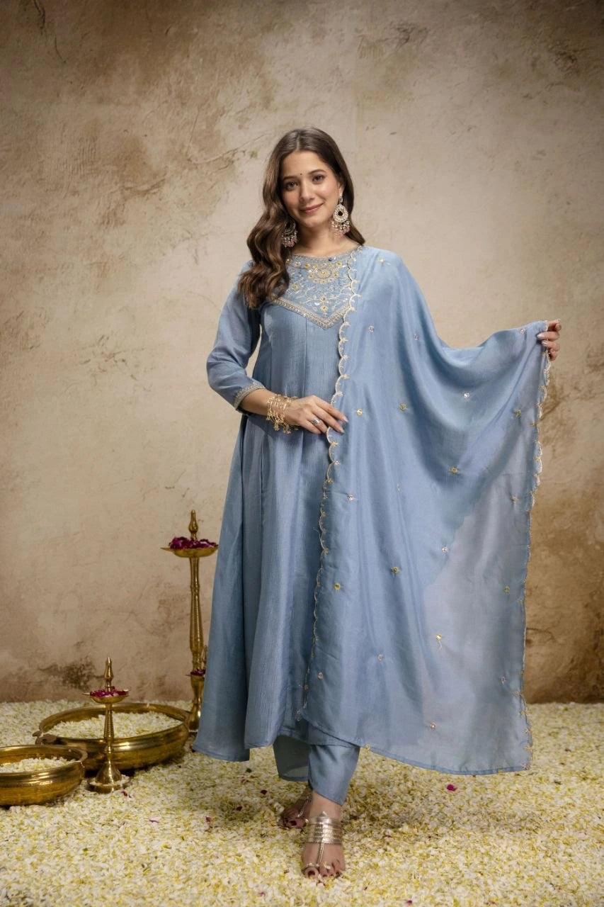 Woman in a light blue traditional outfit with a matching dupatta against a textured beige background.