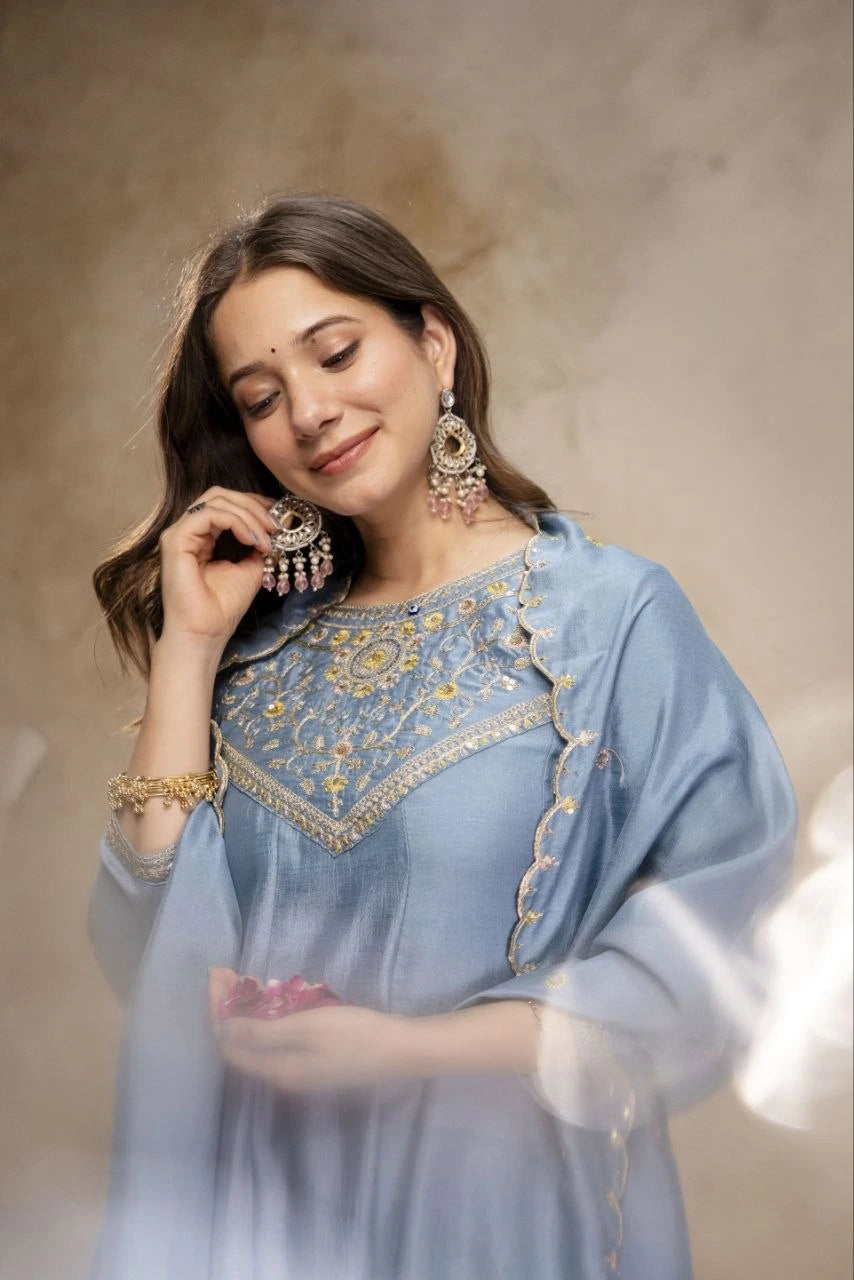 Woman wearing a blue embroidered dress with jewelry against a neutral background
