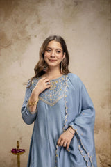 Woman wearing a light blue embroidered traditional outfit against a beige background
