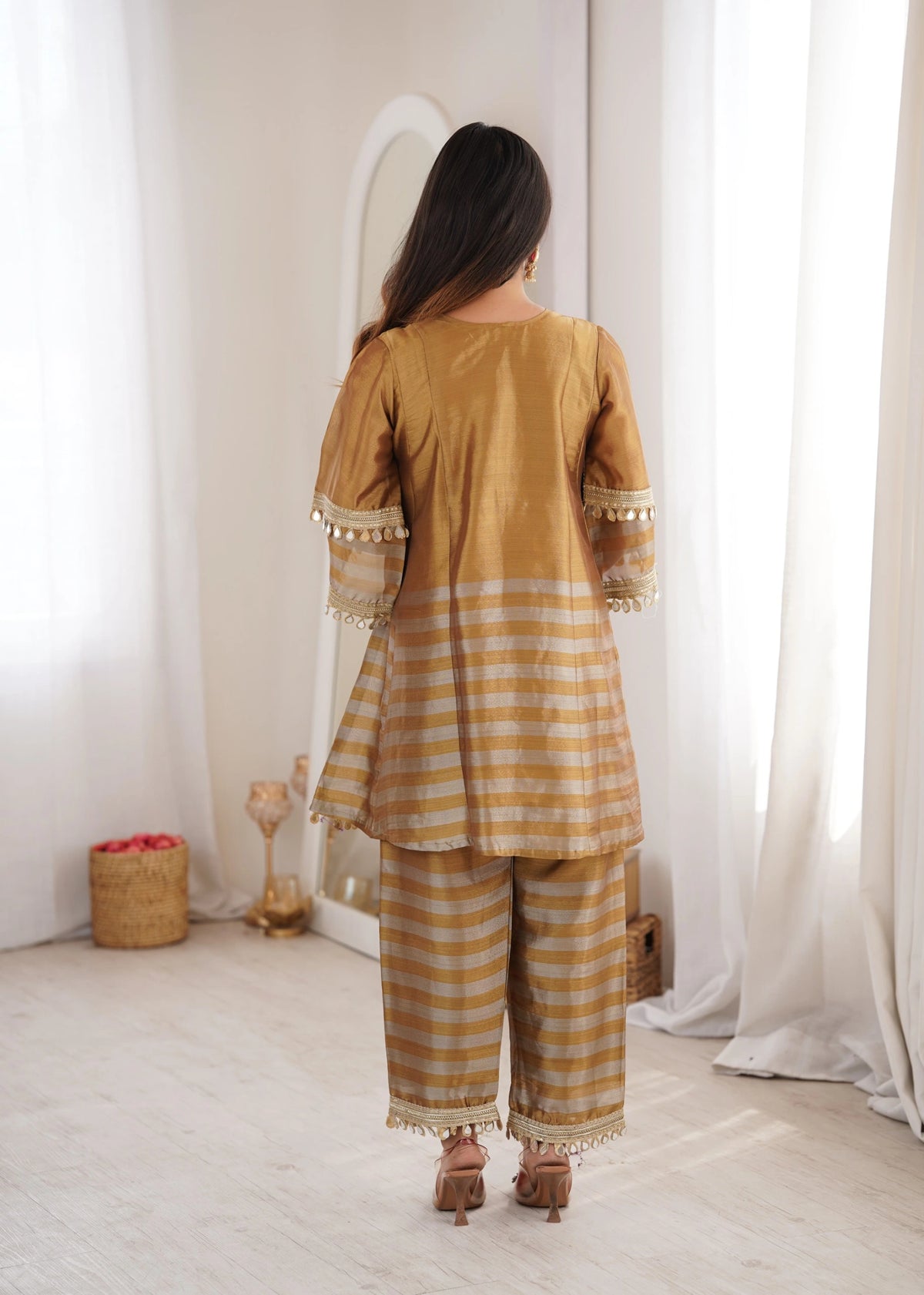 Woman wearing a mustard yellow traditional outfit with white stripes in a minimalistic room.