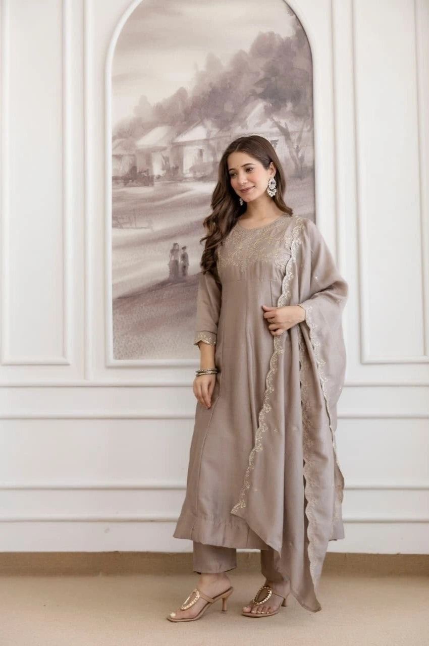 Woman in a beige traditional outfit standing in a room with white walls and an arched window.